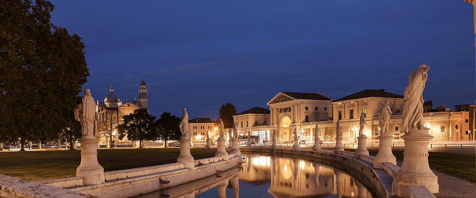 Conference room filled with people seated at a large, curved table, using laptops. Bright ceiling lights illuminate the space, creating a focused atmosphere.